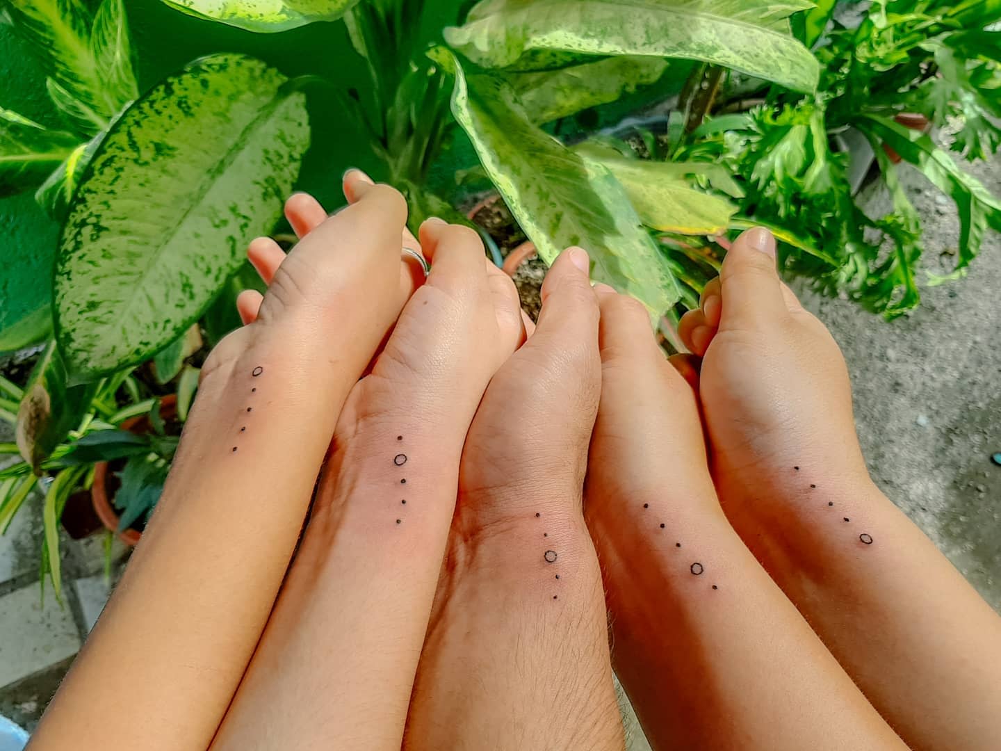 Four forearms with matching minimalist tattoos of dots and circles